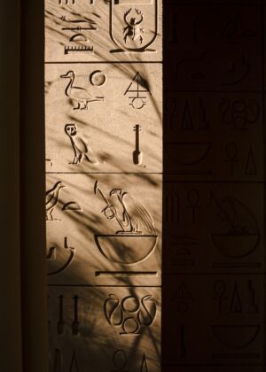 Egyptian hieroglyphs carved into stone with shadows.